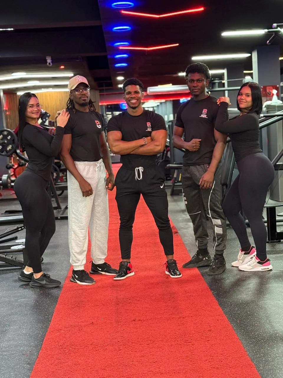 Equipo de Best Gym posando con camisetas negras de la marca sobre la alfombra roja del gimnasio