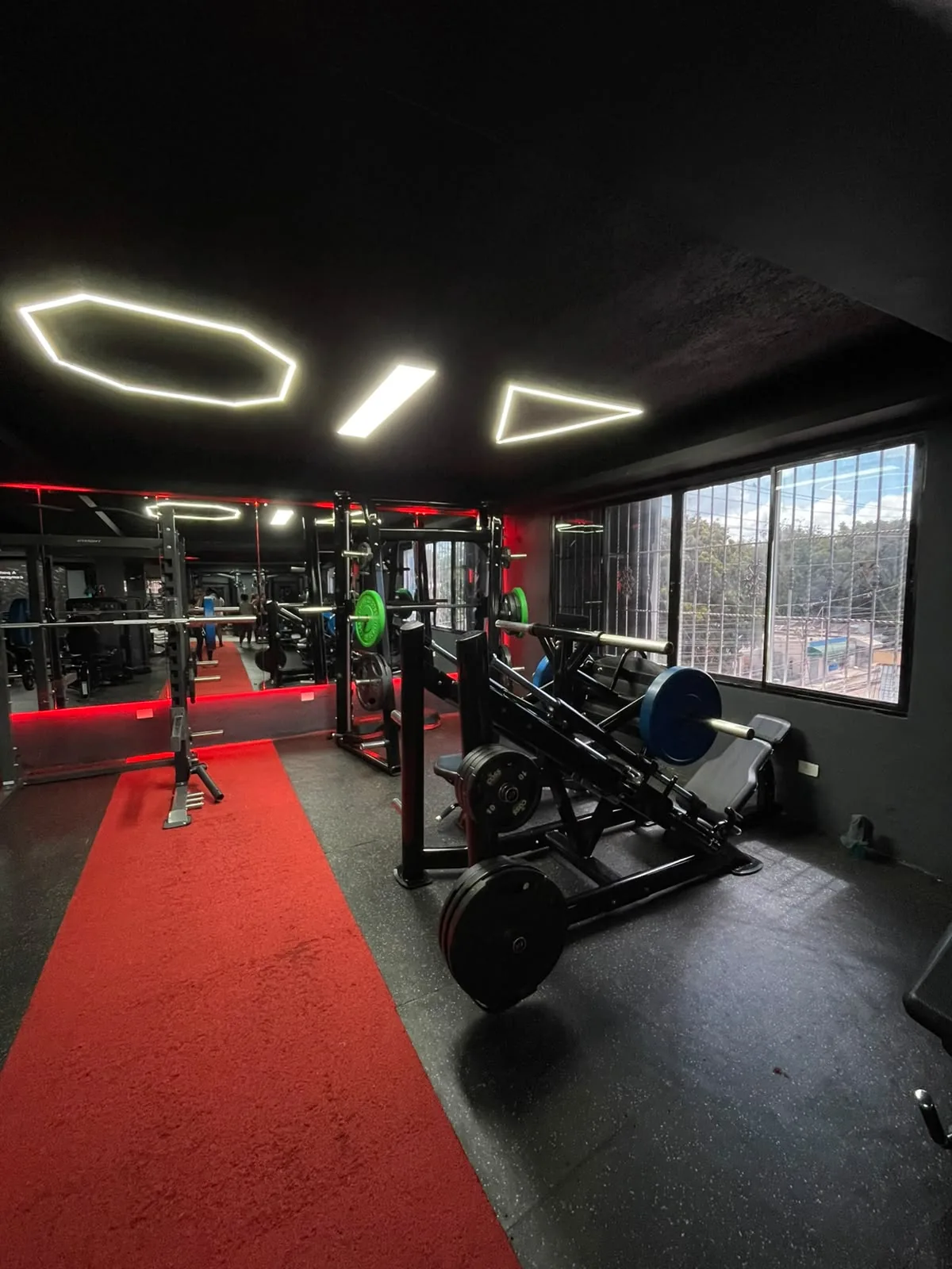 Interior de Best Gym con máquina Smith, prensa de piernas y luces geométricas en el techo